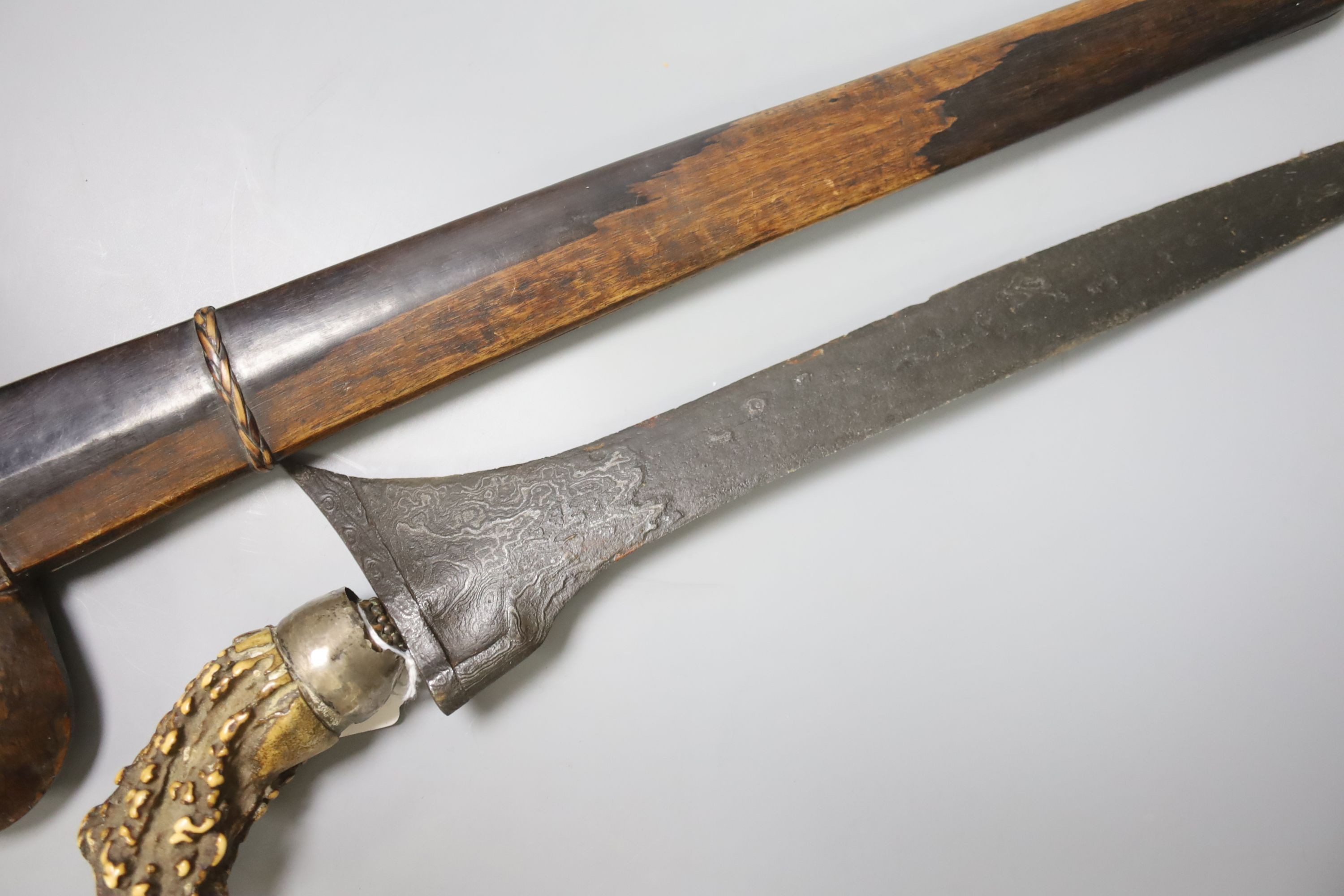 An Indonesian dagger kris, 19th century, earlier swollen black and silver-coloured watered blade, natural staghorn handle, silver cup, wooden scabbard, blade 38cms.